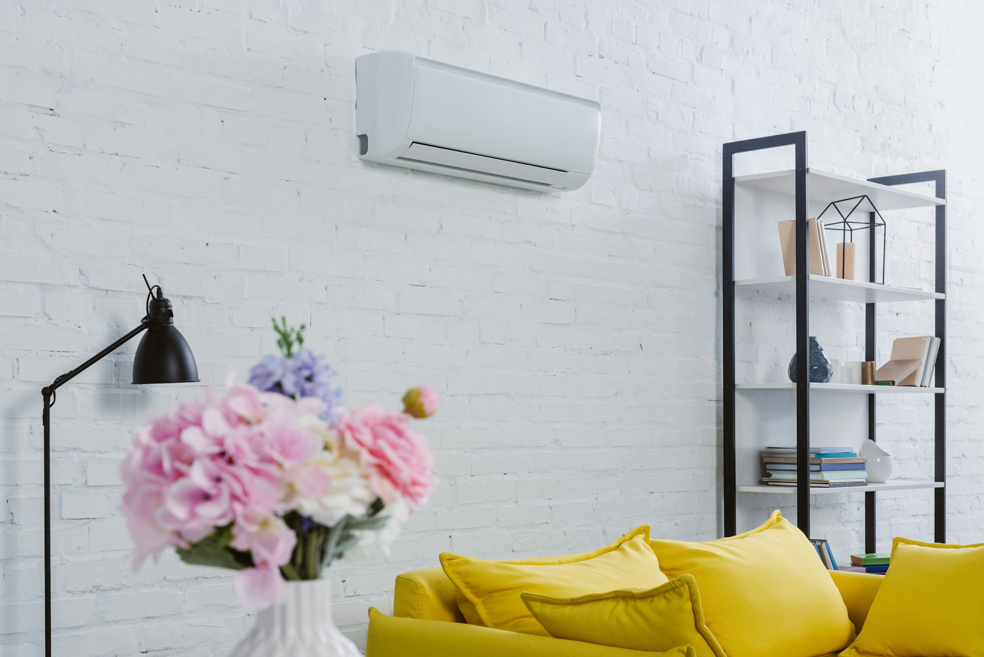 interior of modern living room with flowers in vase, yellow couch and air conditioner hanging on